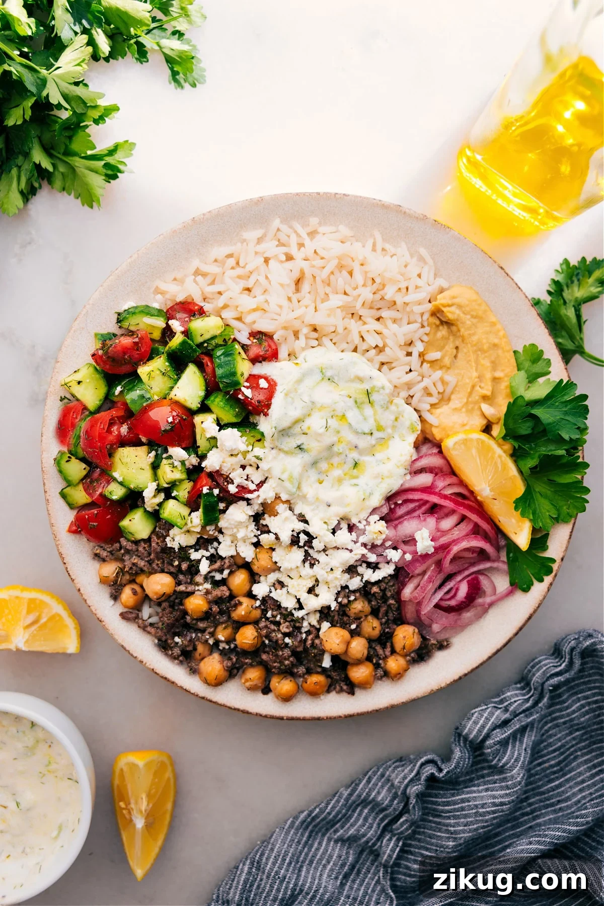 Greek Beef Bowl Greek recipes: A hearty Greek beef bowl loaded with rice and topped with cucumber salad, tzatziki sauce, hummus, and red onions.