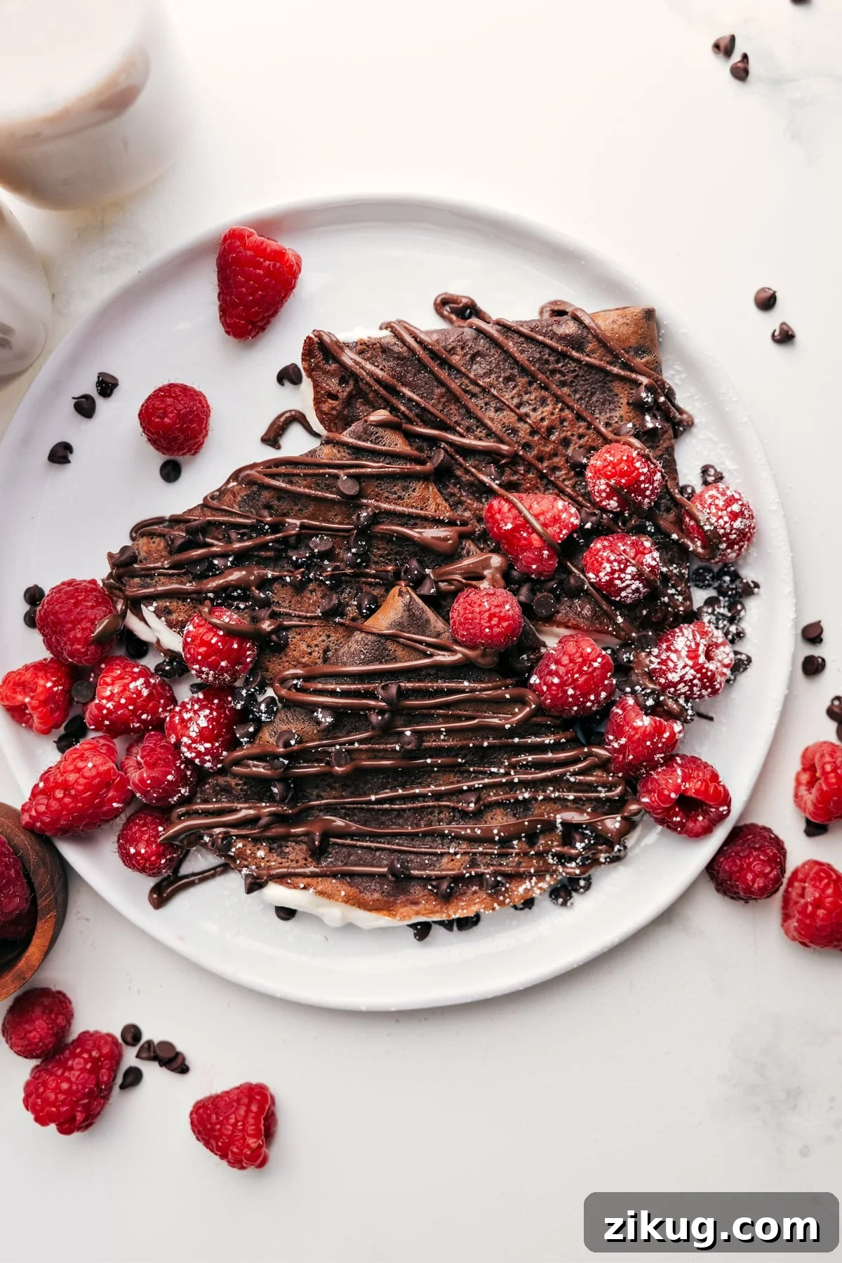 The Ultimate Sweet Treat: Chocolate Crepes Chocolate Crepes topped with chocolate drizzle, mini chocolate chips, fresh berries, and a dusting of powdered sugar on a plate.