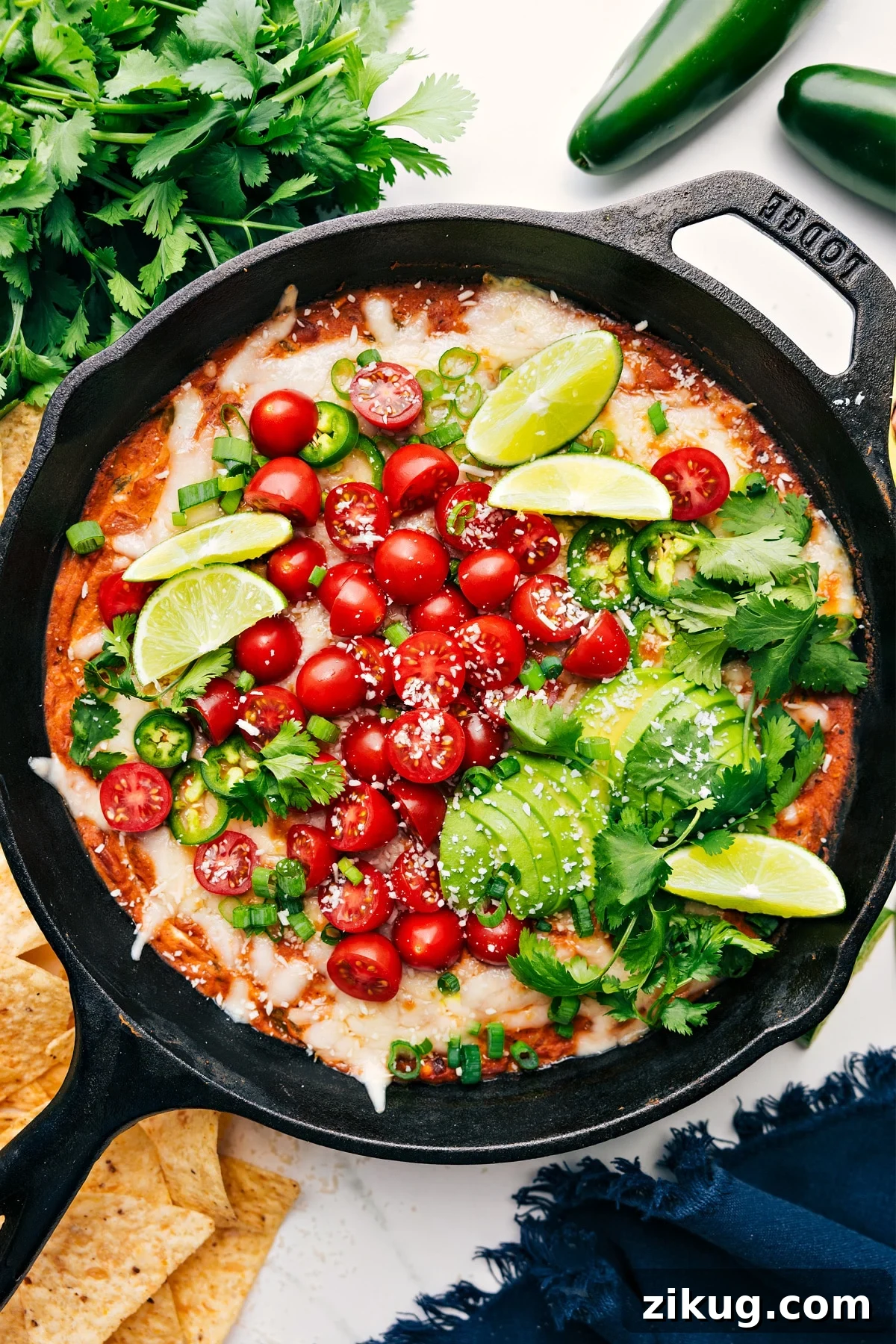 The Perfect Party Dip: Refried Bean Dip Refried Bean Dip in a skillet topped with fresh tomatoes, avocado, lime wedges, green onions, and cilantro.