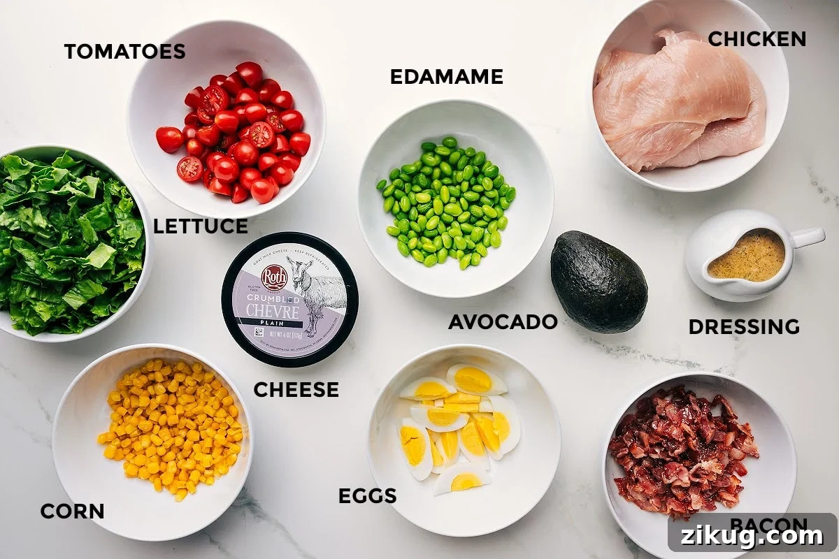 Ingredients In This Cobb Salad Recipe All the ingredients in this recipe prepped out for easy assembly including the lettuce, tomatoes, corn, cheese, edamame, eggs, avocado, dressing, bacon, and chicken.