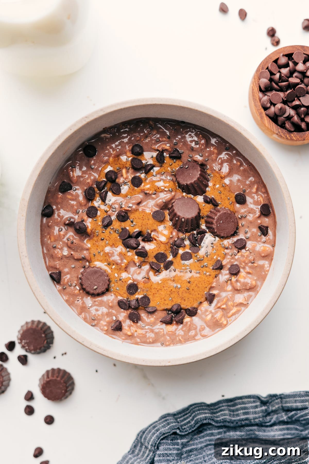 Make-Ahead Chocolate Peanut Butter Overnight Oats 2 Peanut Butter Overnight Oats in a bowl topped with peanut butter, chocolate chips, and Reese’s peanut butter cups.