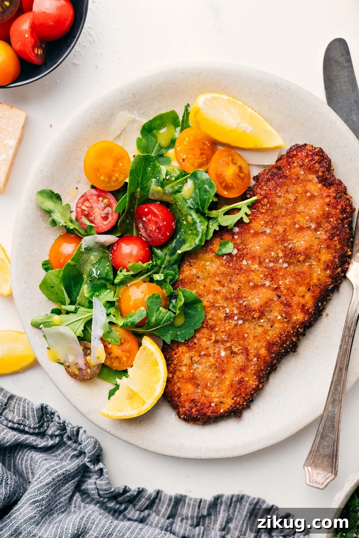 Crispy Chicken Milanese with Lemon Parsley Salad 2 Chicken Milanese on a plate with arugula and tomato salad on the side.
